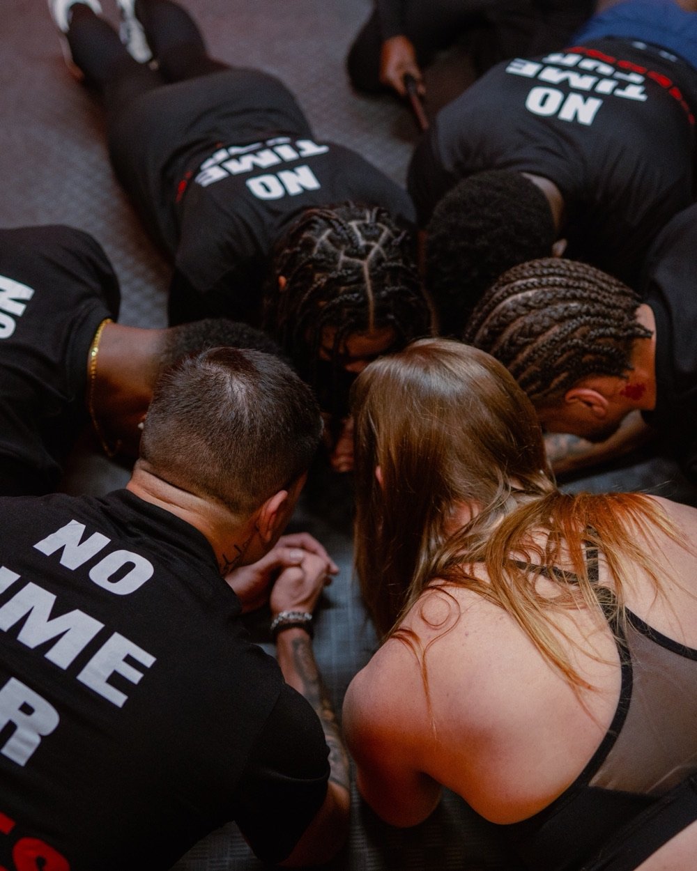 Members in No Time For Tiredness shirts holding a plank together, heads close